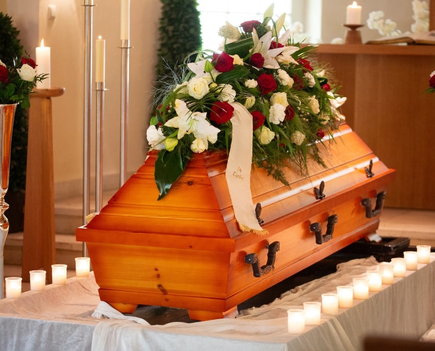 Mit roten und weißen Blumen geschmückter Holzsarg bei einer würdevollen Erdbestattung in einer liebevoll vorbereiteten Trauerhalle