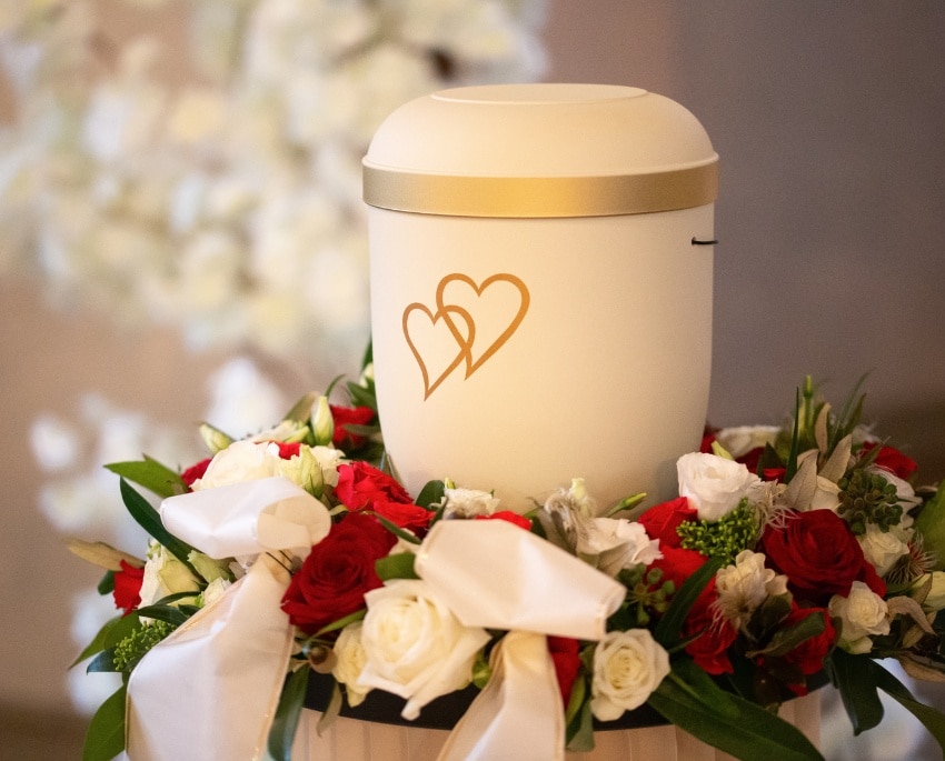 Liebevoll geschmückte Urne mit roten und weißen Blumen bei einer würdevollen Feuerbestattung